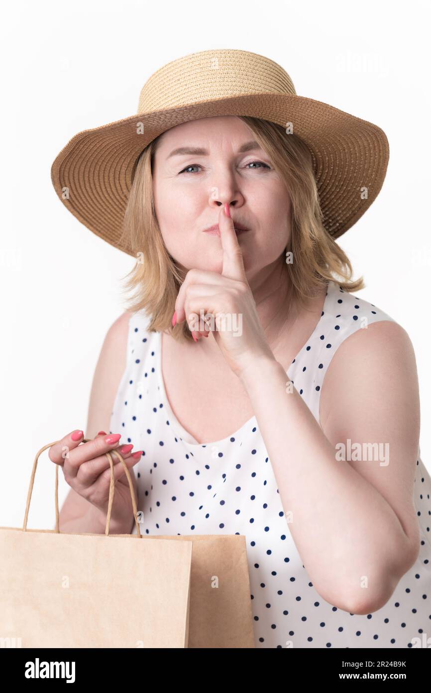 Eine seriöse Käuferin hob ihren Zeigefinger an die Lippen, machte ein geheimes Schild oder bat um Schweigen und hielt eine handwerkliche Einkaufstasche in der anderen Hand Stockfoto