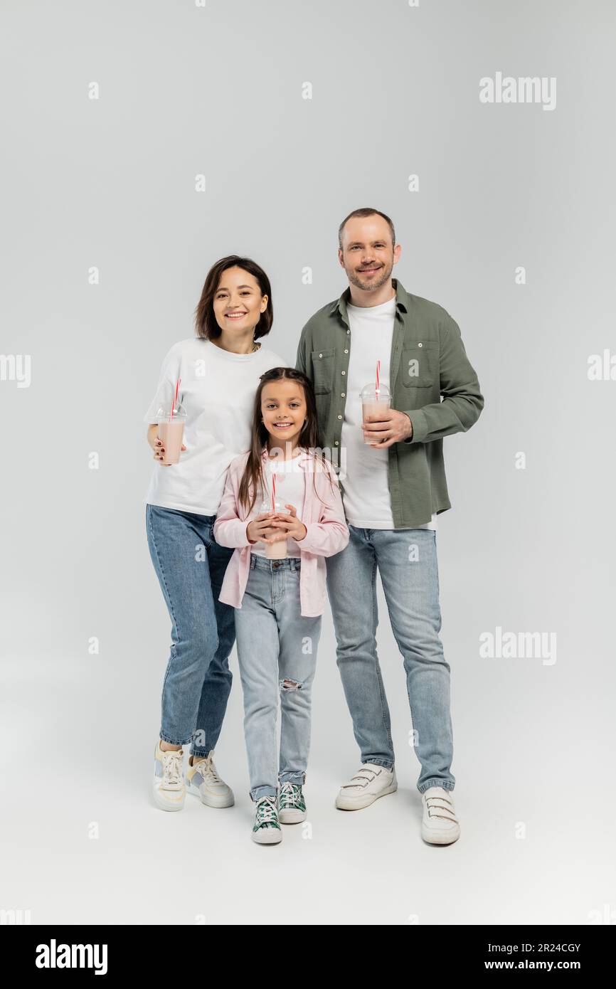 Eine ganze Familie mit lächelnden Kindern und einer Tochter in legerer Kleidung, die Milchshakes in Plastikbechern hält und während des Kindertags in die Kamera schaut Stockfoto