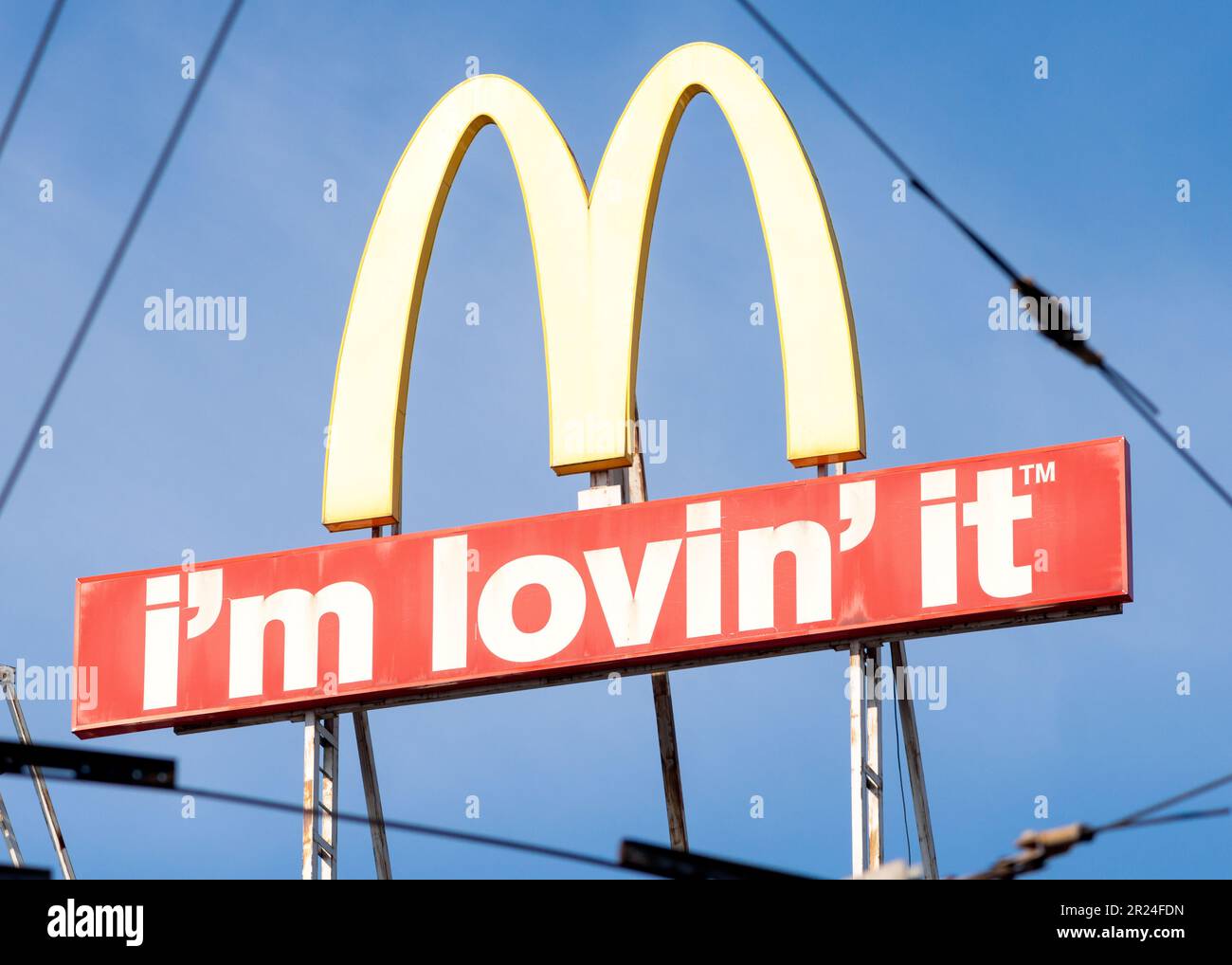 McDonald's Logo-Schild und „I'm Lovin' IT“-Schriftzug Unusual view, gesehen durch Überlandleitungen oder Straßenbahnkabel in städtischer Umgebung Stockfoto