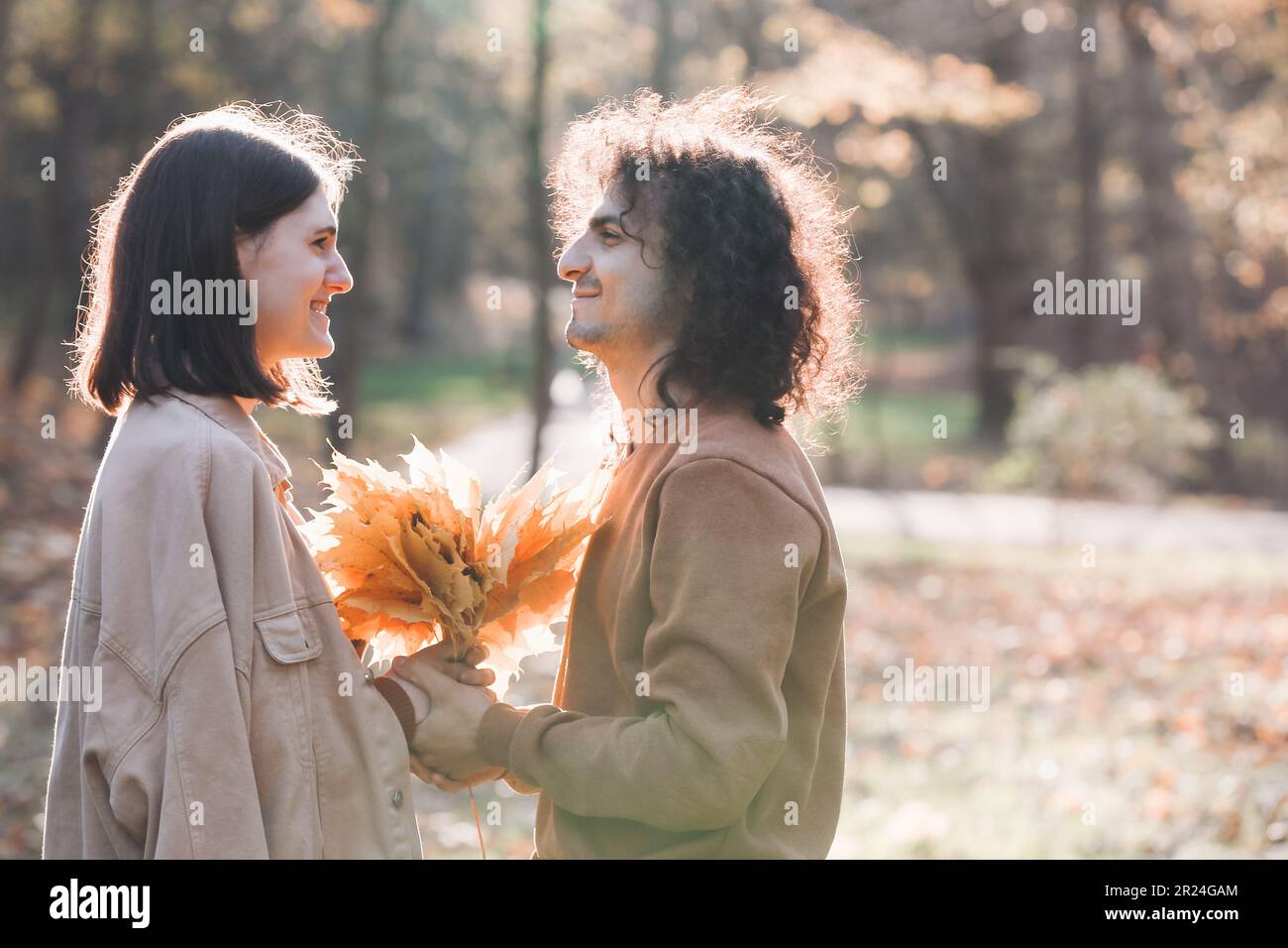 Glückliches junges Paar mit trockenen Blättern, das Zeit zusammen im Herbstpark verbringt, Platz für Text. Dating-Agentur Stockfoto