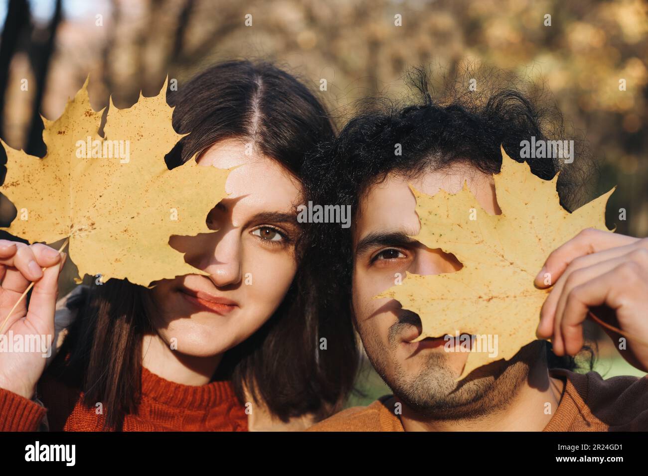 Ein junges Paar, das trockene Blätter in der Nähe seines Gesichts im Freien hält. Dating-Agentur Stockfoto