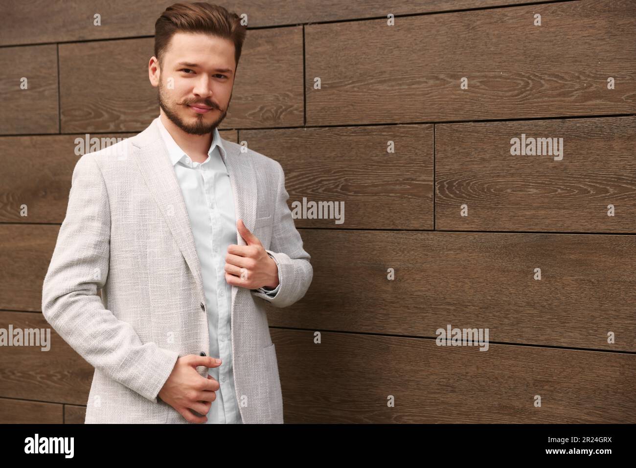 Ein lächelnder Mann im weißen Anzug an der braunen Mauer. Platz für Text Stockfoto