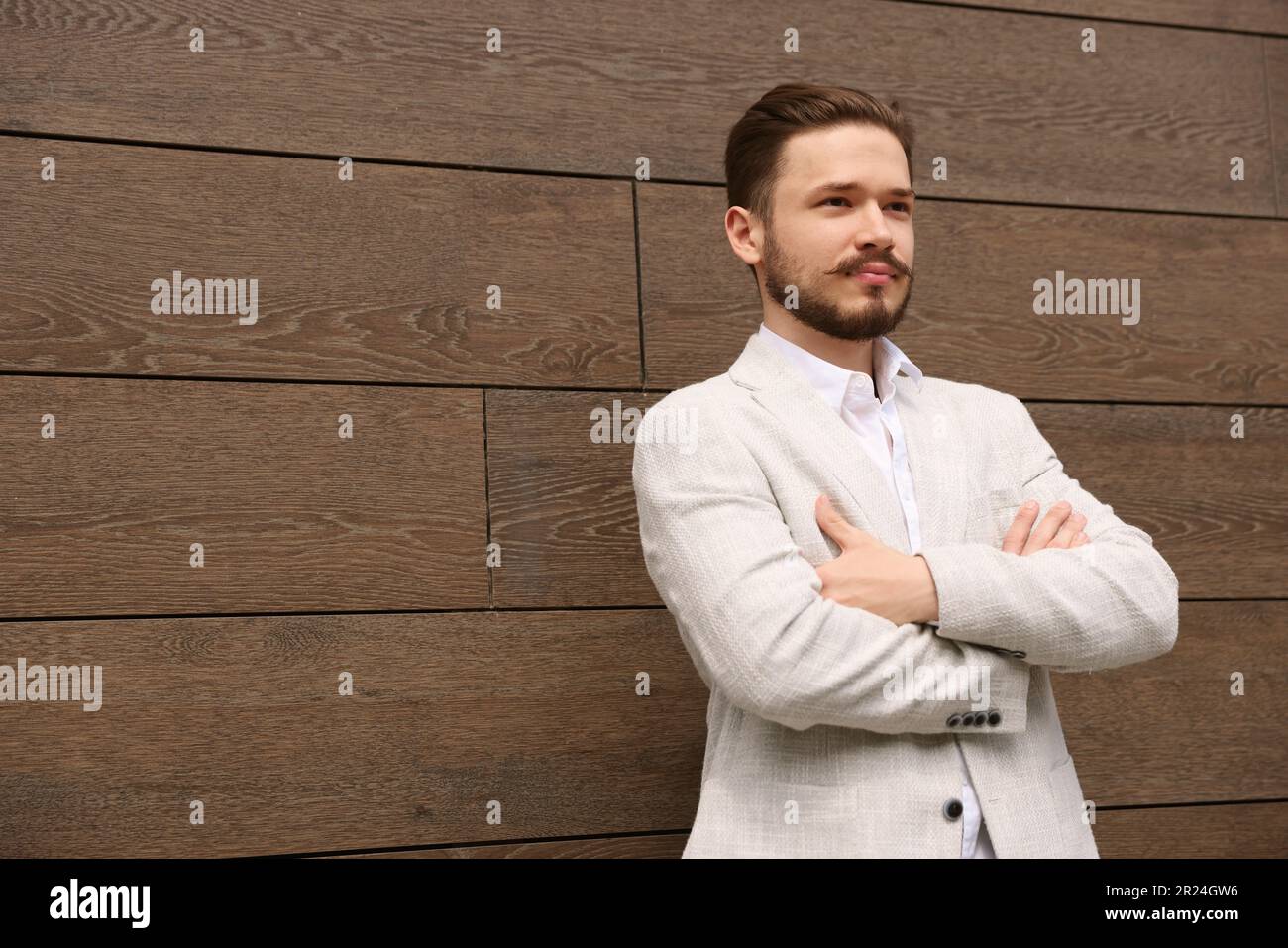 Lächelnder Mann im weißen Anzug, der seine Arme kreuzt, nahe der braunen Mauer. Platz für Text Stockfoto