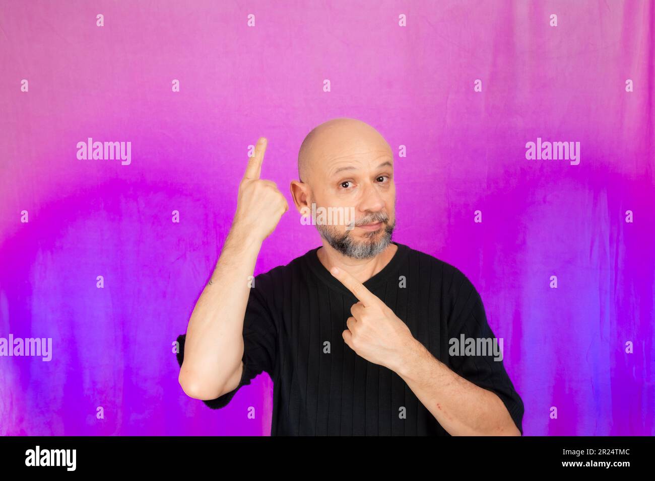 50 Jahre alter Mann, witzig, zeigt mit dem Finger nach oben. Isoliert auf pinkfarbenem Hintergrund. Stockfoto
