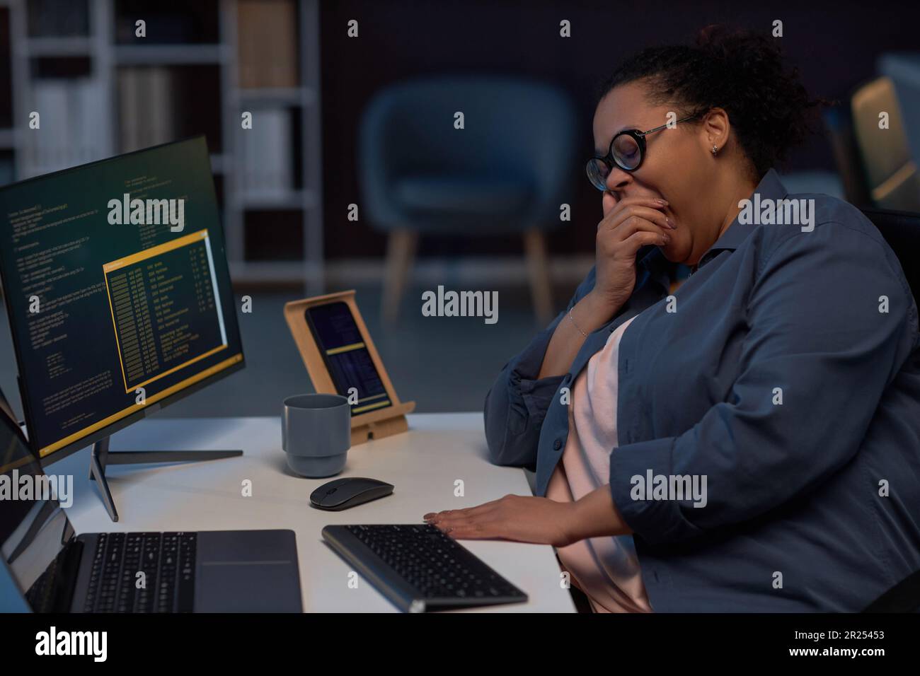Müde Programmierer, die während der Arbeit an ihrem Arbeitsplatz am Computer gähnt, bis spät in die Nacht während der Deadline Stockfoto