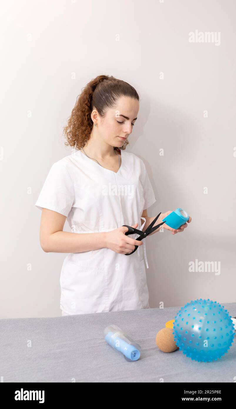 Rehabilitationsspezialist, Physiotherapeut Mit Rehab-Tools Schneidet Elastisches Kinesiologisches Band Mit Schere Im Therapieraum. Vertikale Ebene Stockfoto