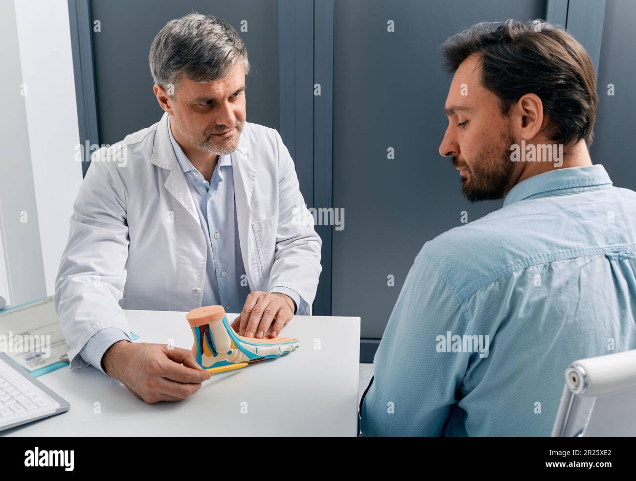 Behandlung von Plattfüßen. Podiatrist-Arzt als Berater eines erwachsenen Patienten mit Plattfuss, Erläuterung der Behandlungsmethoden mit Hilfe des anatomischen pes-planus-Modells Stockfoto