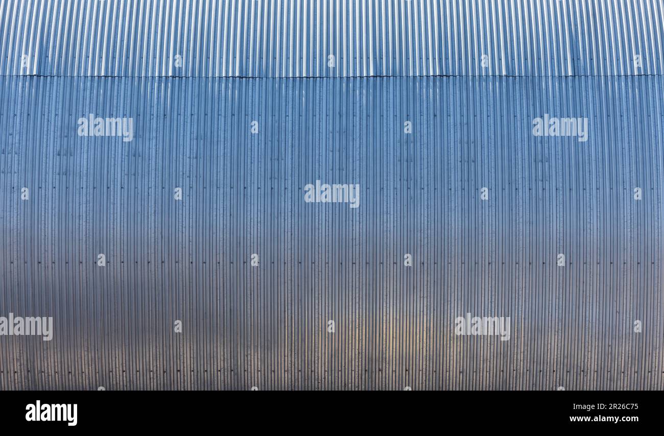 Glänzend gebogene, gerippte Metallwand eines Lagergebäudes, moderne industrielle Architektur im Hintergrund Fotostruktur Stockfoto