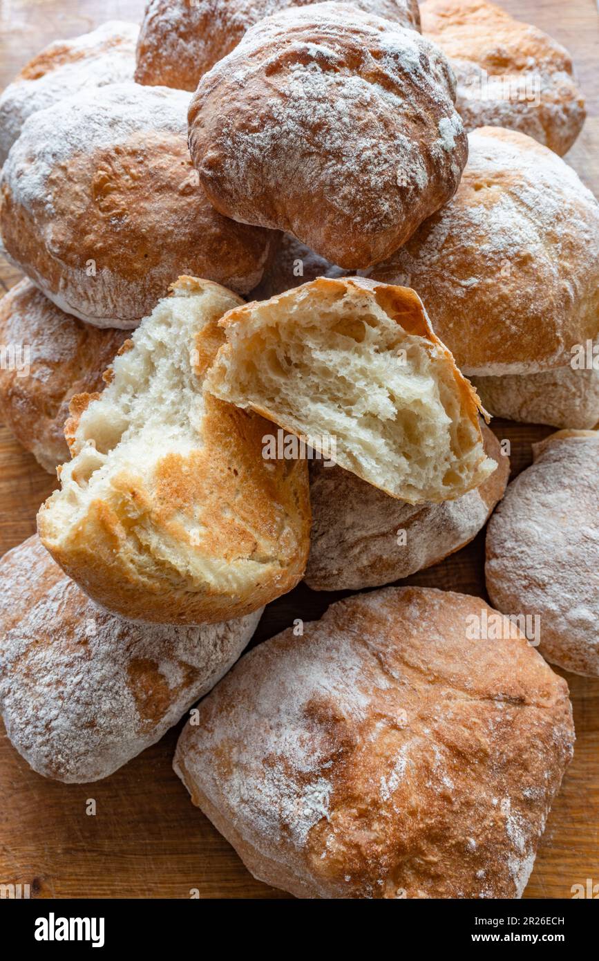 Ein Haufen frisch gebackener, weißer, verkrusteter, hausgemachter Ciabatta-Rollen auf einem rustikalen Holztisch, Draufsicht, Seitenansicht. Stockfoto