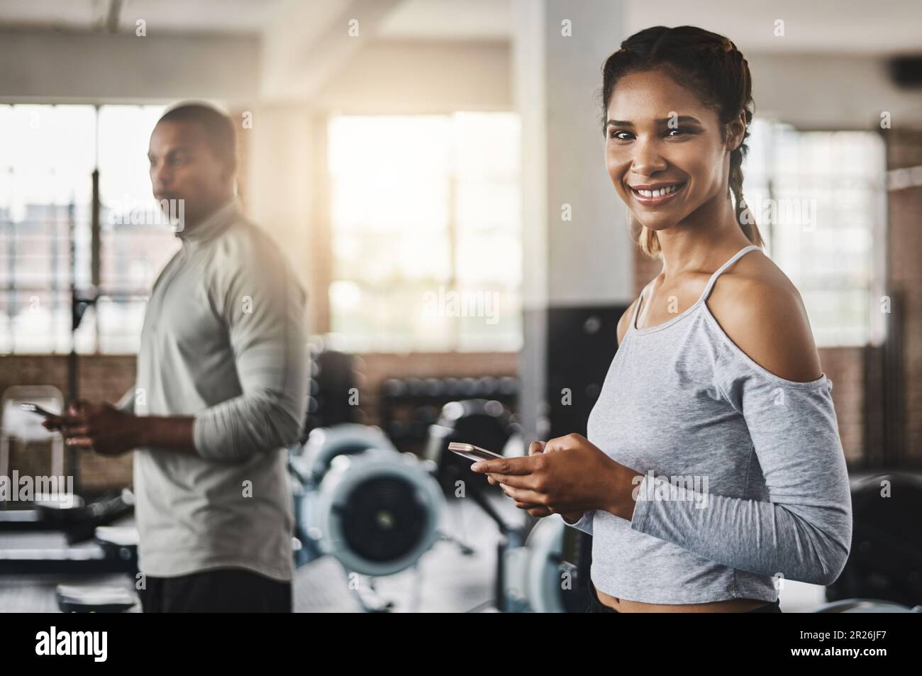 Es war noch nie so einfach, mein Workout im Auge zu behalten. Eine junge Frau, die ein Handy im Fitnessstudio benutzt. Stockfoto