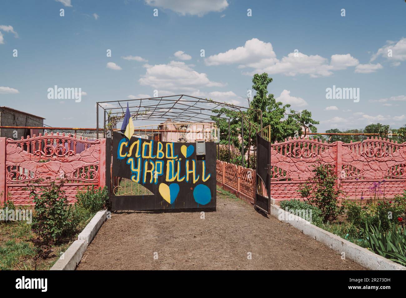 Krieg in der Ukraine. Der Zaun eines Hauses, zerstört durch Beschuss auf dem Land. Übersetzung der Inschrift auf dem Zaun - Ruhm für die Ukraine Stockfoto