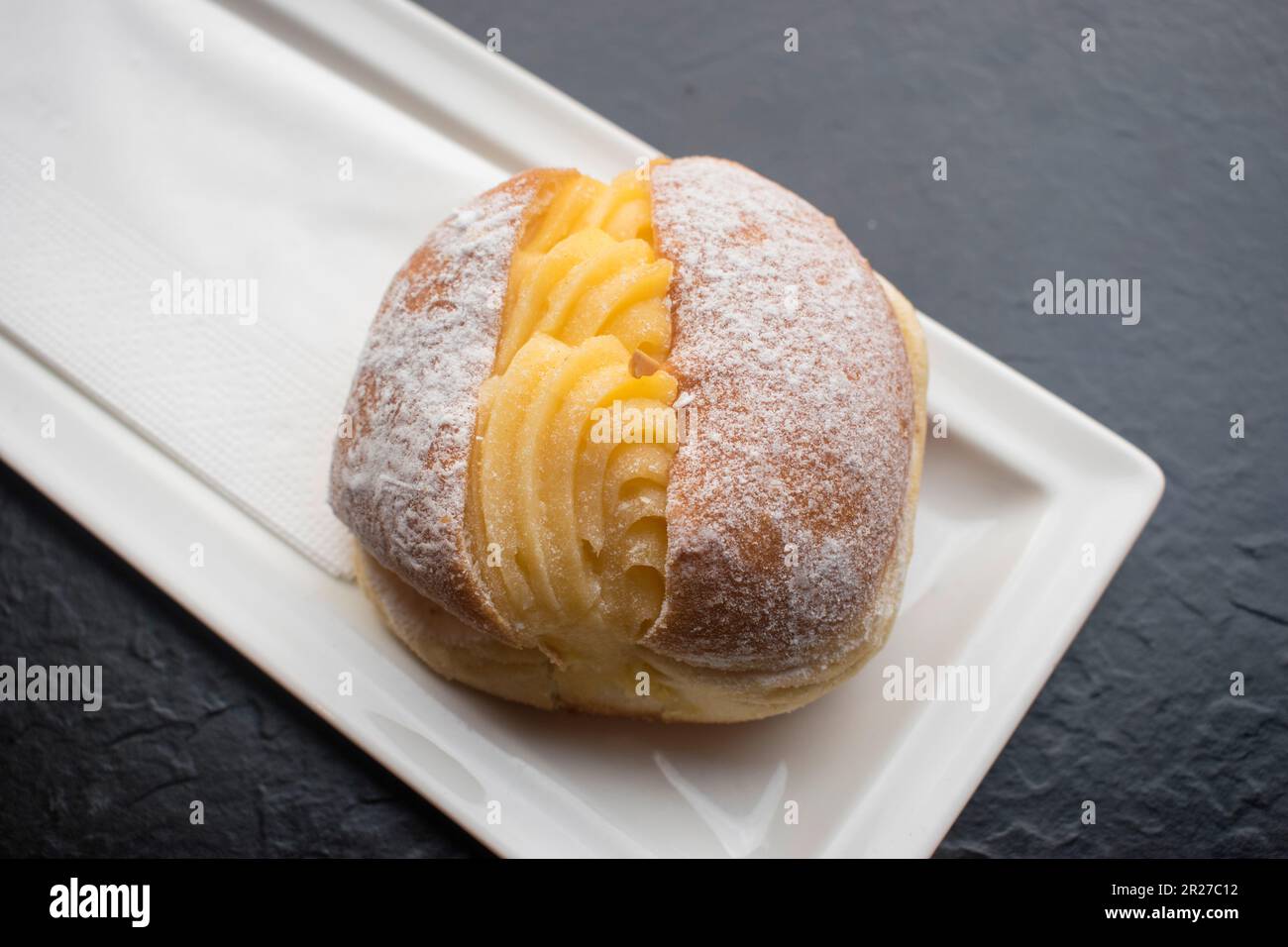 Portugiesischer Donut oder Berliner mit Eiercreme auf einem weißen Teller. Es besteht aus einem gebratenen süßen Teig gefüllt mit Sahne und Zucker. Stockfoto
