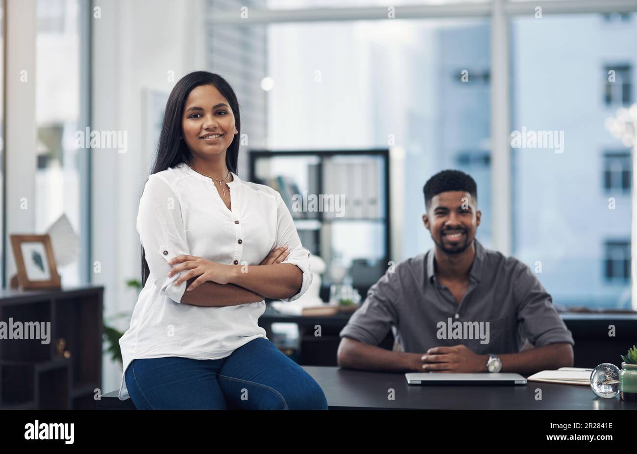 Ich fühle mich hier zugehörig. Porträt einer jungen Geschäftsfrau in einem Büro mit ihrem Kollegen im Hintergrund. Stockfoto