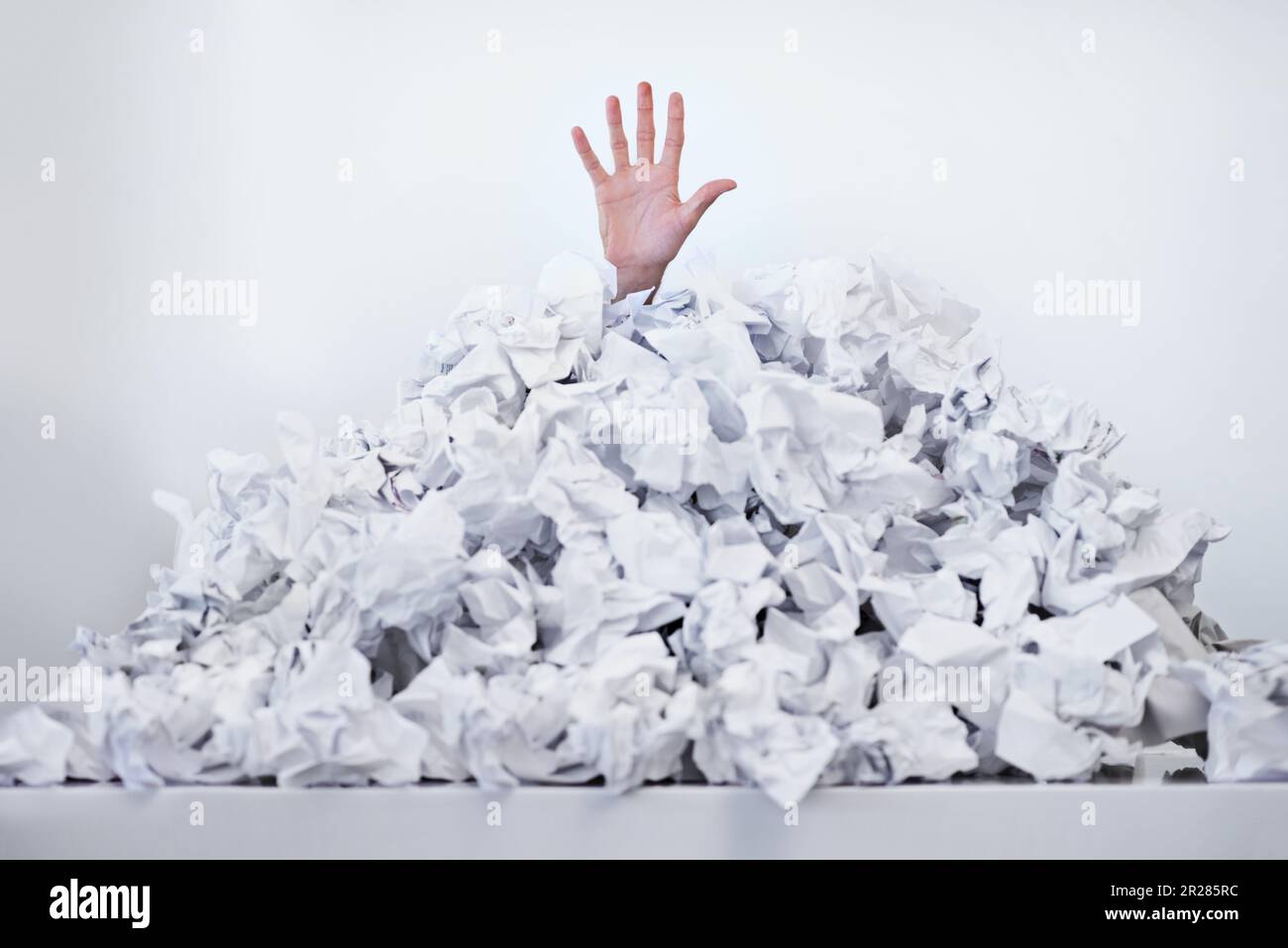 Helfen Sie mir, im Papierkram zu ertrinken. Eine Hand, die unter einem Stapel Papiere nach oben greift. Stockfoto