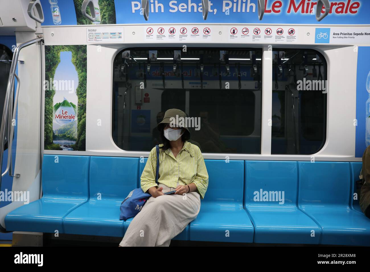 Junge Indonesierin, die eine Maske in einem leeren Mass Rapid Transit-Wagen trägt und in Jakarta, Indonesien, einen Werbespot von Le Minerale über dem Kopf zeigt Stockfoto