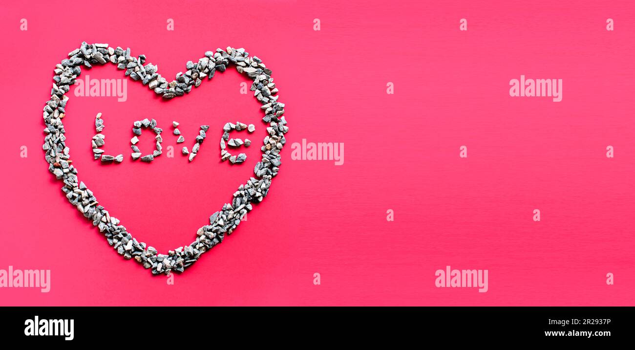 Das Herzsymbol und der Buchstabe LIEBE im Herzen bestehen aus kleinen Steinen oder Kieseln auf rotem Hintergrund. Es ist ein Konzept des Tages der Liebe Stockfoto