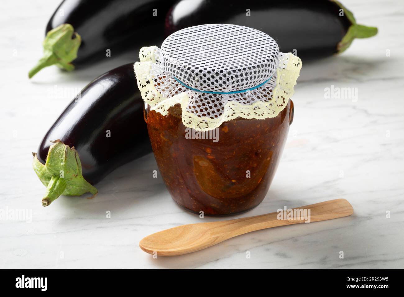 Glasbehälter mit hausgemachtem Auberginen-Chutney und frischen violetten Auberginen an der Seite Stockfoto