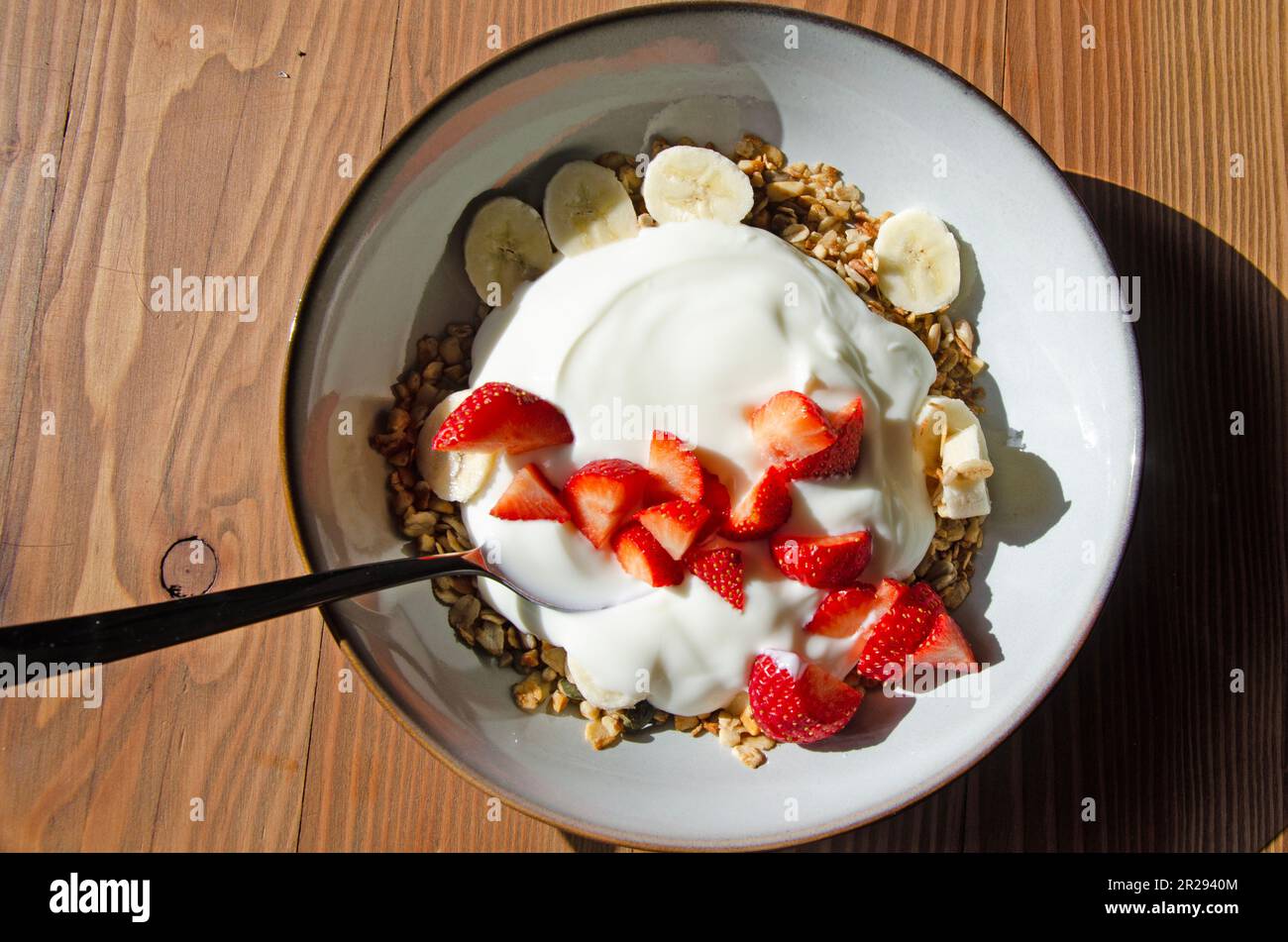 Frische Erdbeeren, Bananen, Müsli und Joghurt auf einem hölzernen Tisch Stockfoto