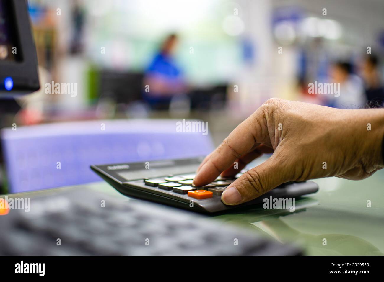 Nahaufnahme eines Mannes Finger, der einen Taschenrechner auf einen Glastisch in einem Büro drückt, um die Zinsen für Kunden zu berechnen, die einen Kredit benötigen, verschwommen Ba Stockfoto