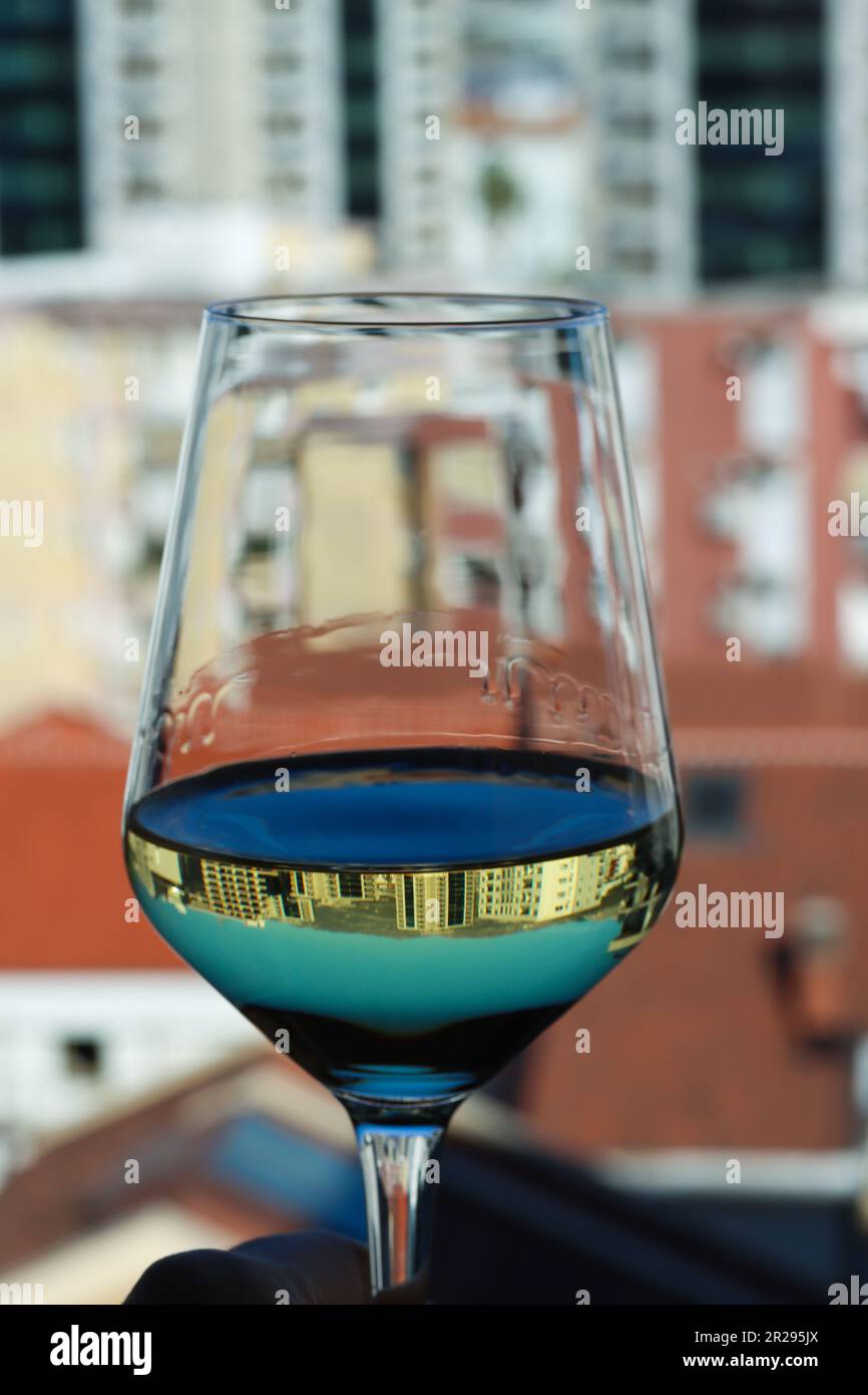 Ein Glas Weißwein mit Blick auf die Stadt. Reflexion der Stadt im Glas Weißwein. Nahaufnahme eines transparenten Glases Weißwein vor dem Stockfoto