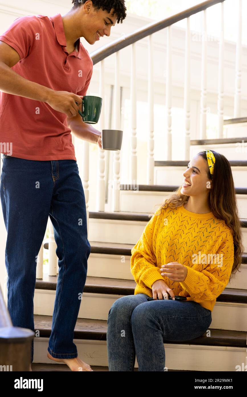 Glückliches, vielseitiges Paar, das Kaffee trank und zu Hause auf der Treppe saß Stockfoto