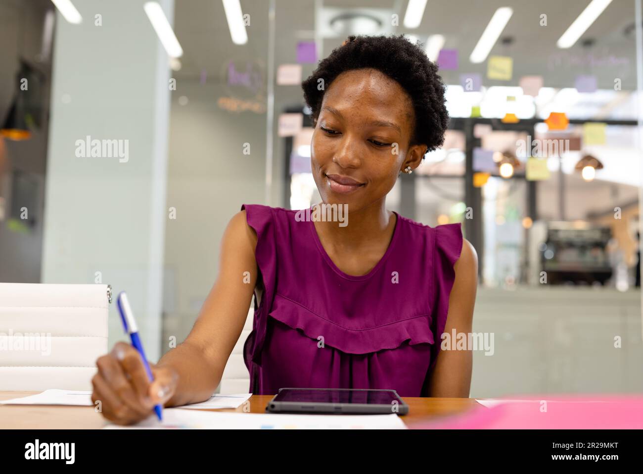 Porträt einer afroamerikanischen Geschäftsfrau, die auf Papier mit einem digitalen Tablet am Schreibtisch im Büro schreibt Stockfoto