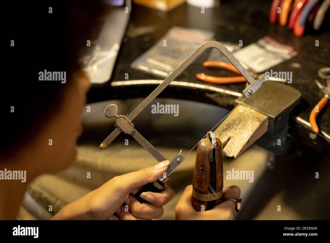 Birassische Mitarbeiterin, die Schmuck mit Werkzeugen in der Schmuckwerkstatt herstellt Stockfoto