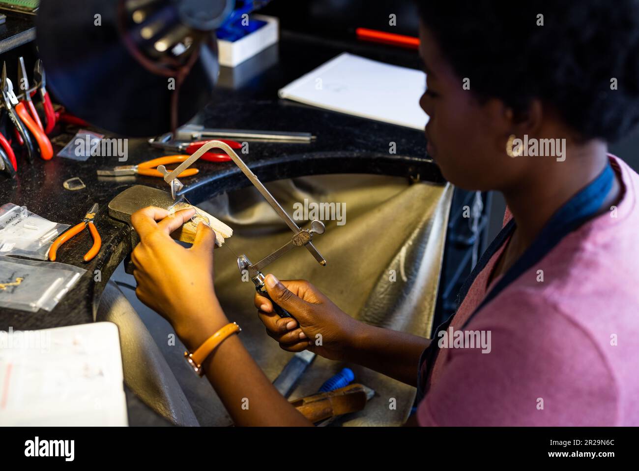afroamerikanische Mitarbeiterin, die Schmuck mit Werkzeugen in einer Schmuckwerkstatt herstellt Stockfoto