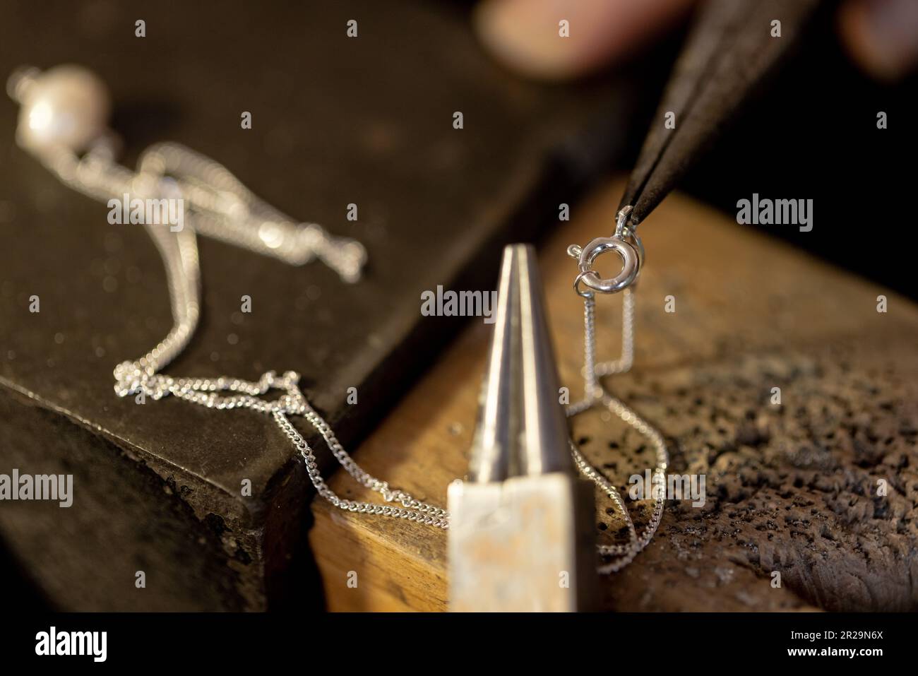 Nahaufnahme der Hände einer birassischen Arbeiterin, die Schmuck mit Werkzeugen in einer Schmuckwerkstatt herstellt Stockfoto