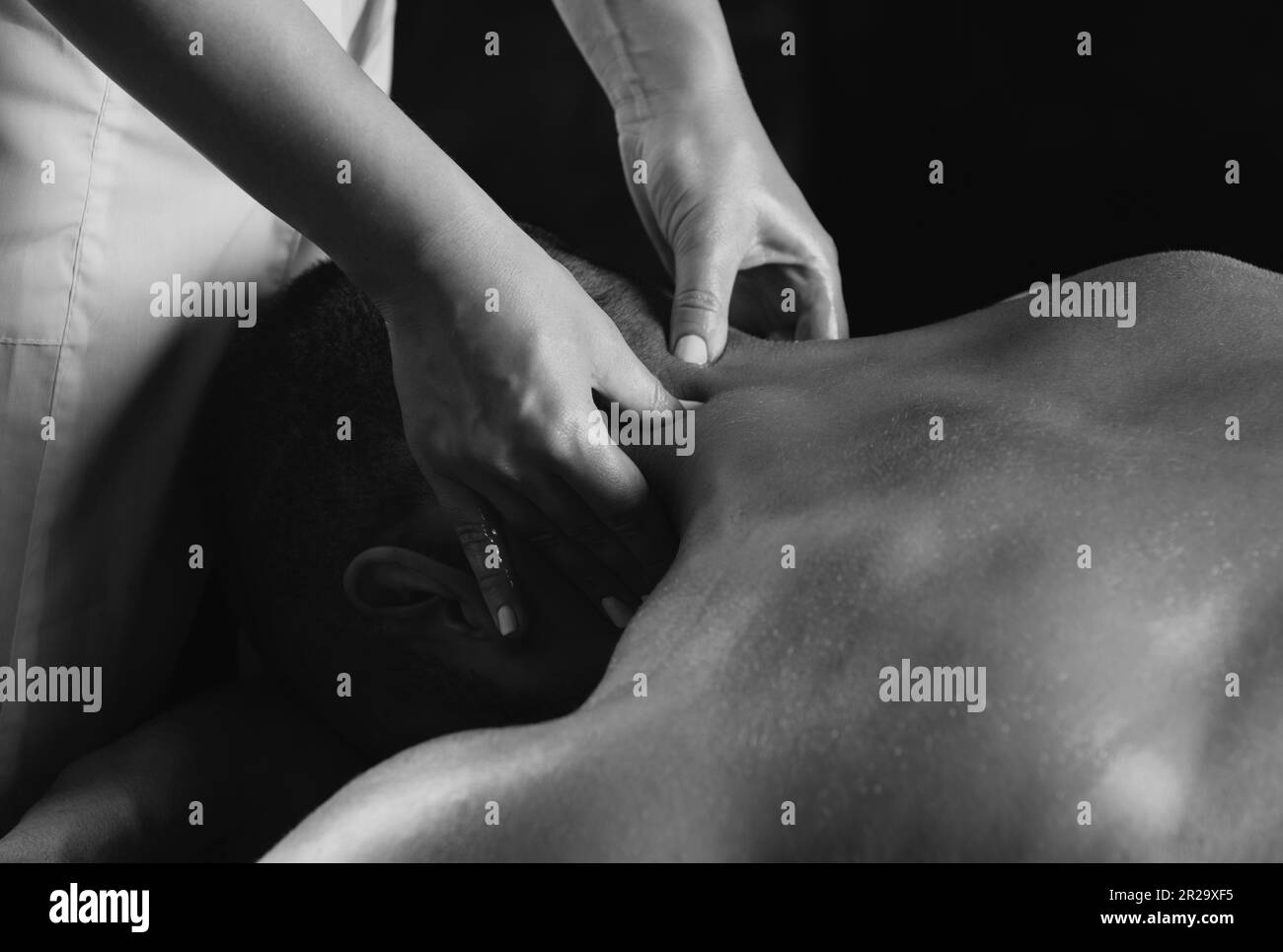Massagen für Männer aus nächster Nähe. Physiotherapeut massiert männlichen Hals. Ein Mann, der sich auf dem Massagetisch entspannt und sich massiert. Stockfoto