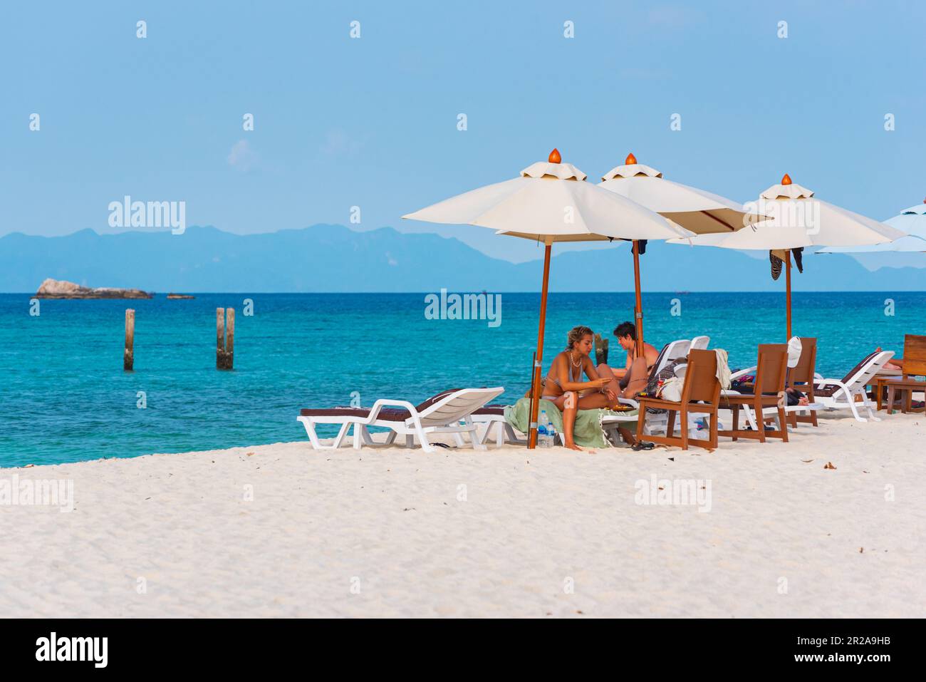 Ko Lipe, Thailand - 9. April 2023: Reisende entspannen sich auf Sonnenliegen unter Sonnenschirmen am Sunrise Beach. Stockfoto