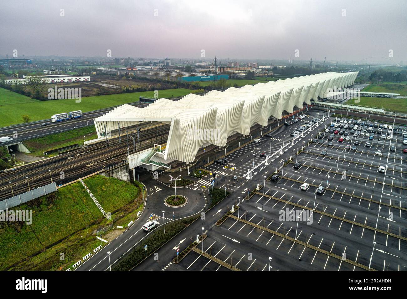 Luftaufnahme des Bahnhofs Reggio Emilia AV Mediopadana. Ein- und Ausstieg aus Zügen. Verkehr auf der Autobahn A1. Reggio Emilia, Emilia Romagna, Italien, Stockfoto