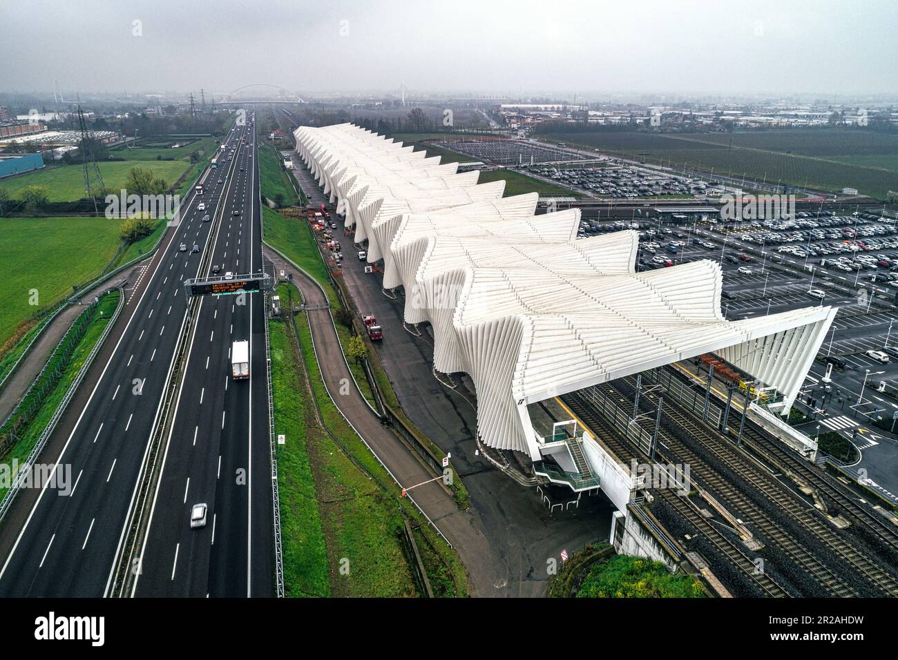 Luftaufnahme des Bahnhofs Reggio Emilia AV Mediopadana. Ein- und Ausstieg aus Zügen. Verkehr auf der Autobahn A1. Reggio Emilia, Emilia Romagna, Italien, Stockfoto