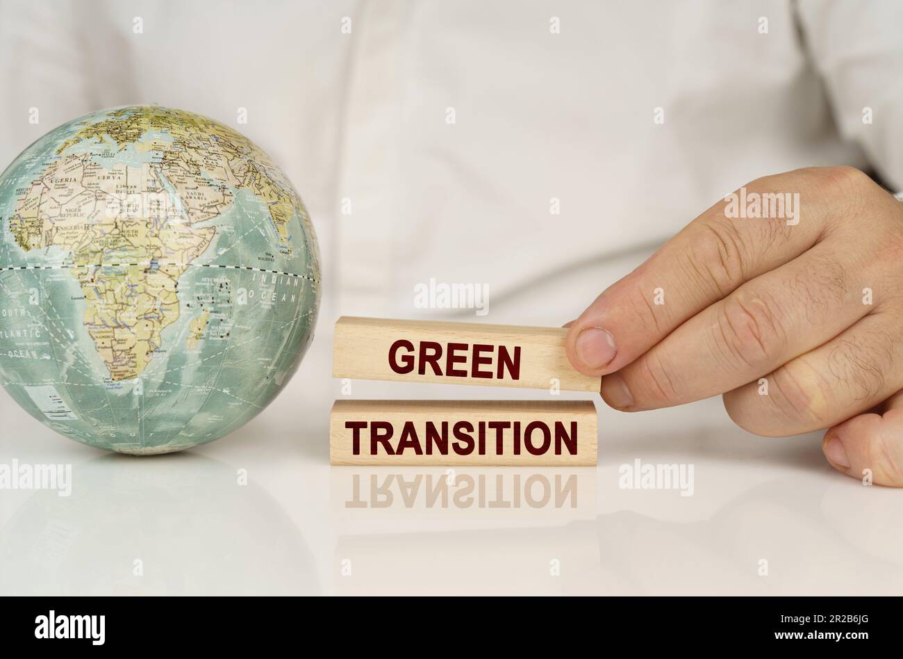 Auf einer weißen reflektierenden Oberfläche befindet sich ein Globus in den Händen von Holzblöcken mit der Aufschrift „Grüner Übergang“. Das Konzept von Industrie und Umwelt Stockfoto