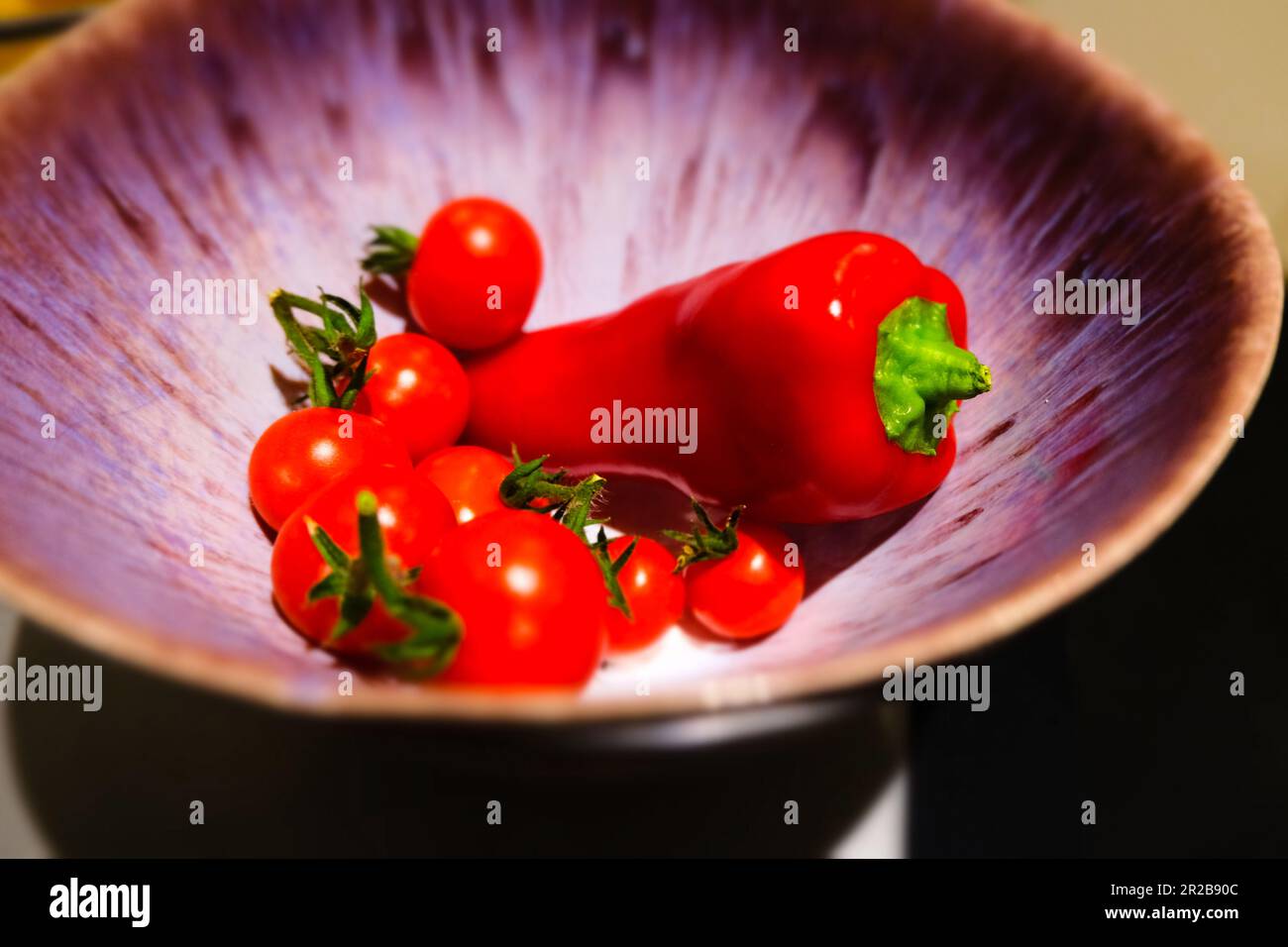 Reife Tomaten und lebendige Paprika schmiegen sich in einer Schüssel zusammen und schaffen ein farbenfrohes und appetitliches Schauspiel. Ihr frisches Aroma und ihre knackige Textur. Stockfoto