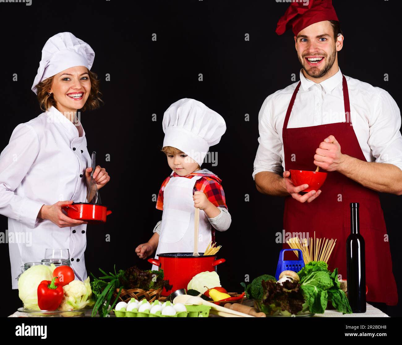 Kind mit Eltern, die in der Küche kochen. Glückliche Familie bereitet Frühstück oder Abendessen zusammen zu. Hausgemachtes Essen. Eltern, die dem kleinen Jungen das Kochen beibringen Stockfoto