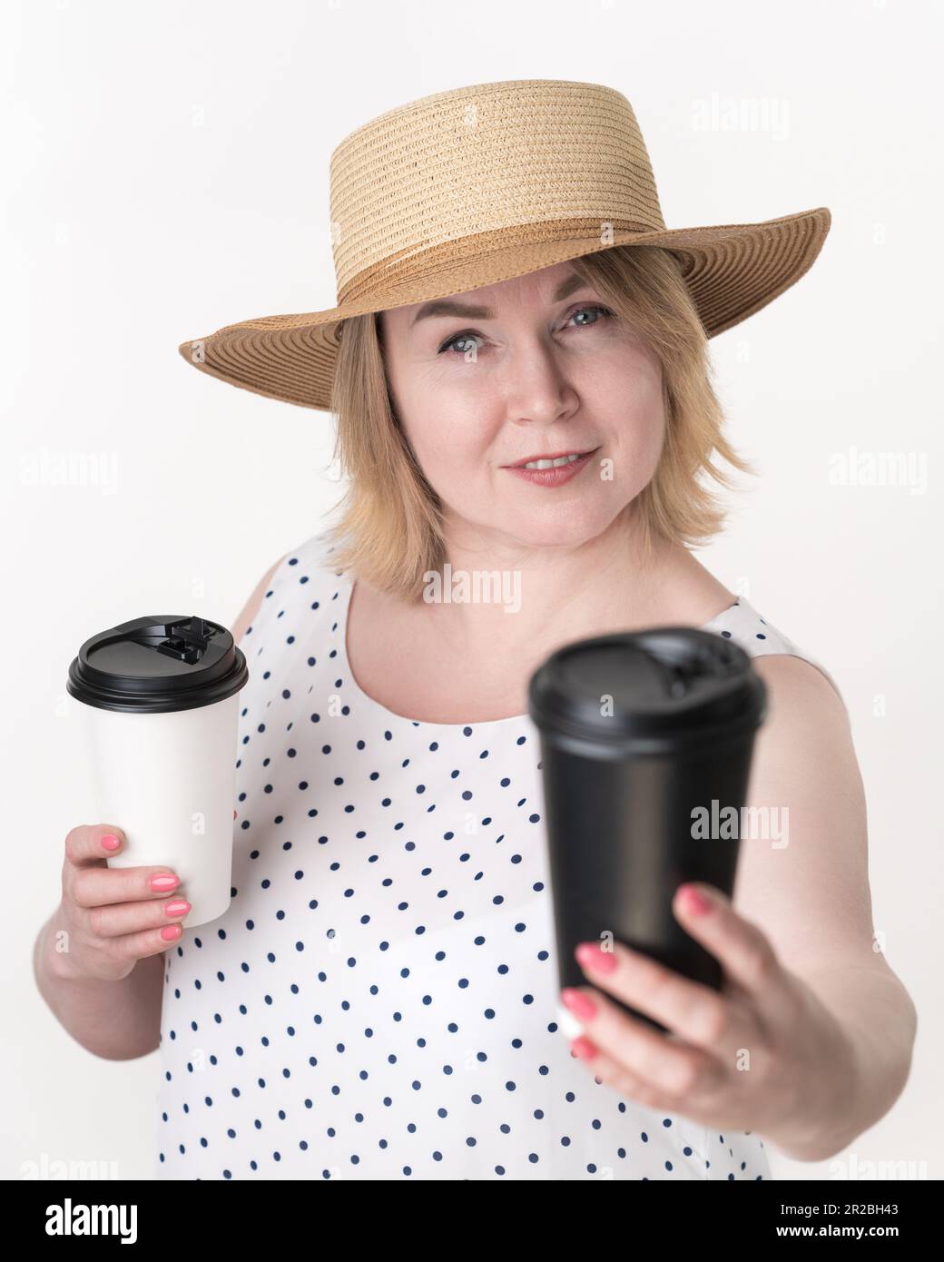 Blonde Frau, die schwarz-weißen Einwegbecher für Kaffee in verschiedenen Händen hält. Auswahlkonzept. Porträt der erwachsenen Frau mittleren Alters Stockfoto