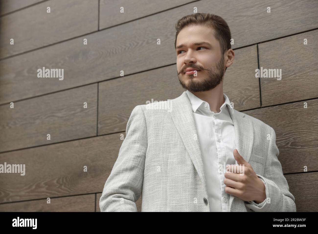 Ein hübscher Mann im weißen Anzug in der Nähe einer braunen Ziegelmauer. Platz für Text Stockfoto