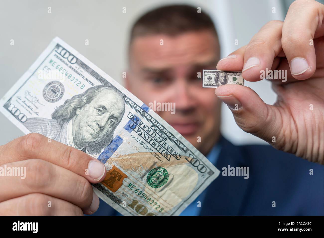 Ein junger Geschäftsmann hält eine kleine Rechnung in der Hand, als Symbol für sinkende Einkommen. Das Konzept des kleinen Gehalts. Ein trauriges Gesicht. Dollarinflation Stockfoto