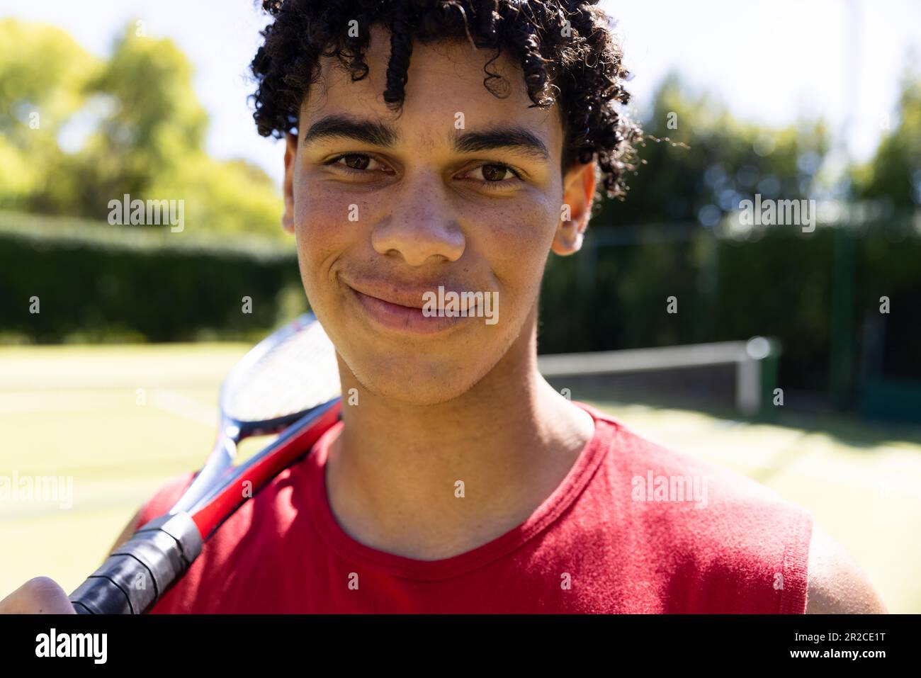 Porträt eines lächelnden, geschlechtsreifen Mannes mit Tennisschläger auf einem sonnigen Tennisplatz im Freien Stockfoto