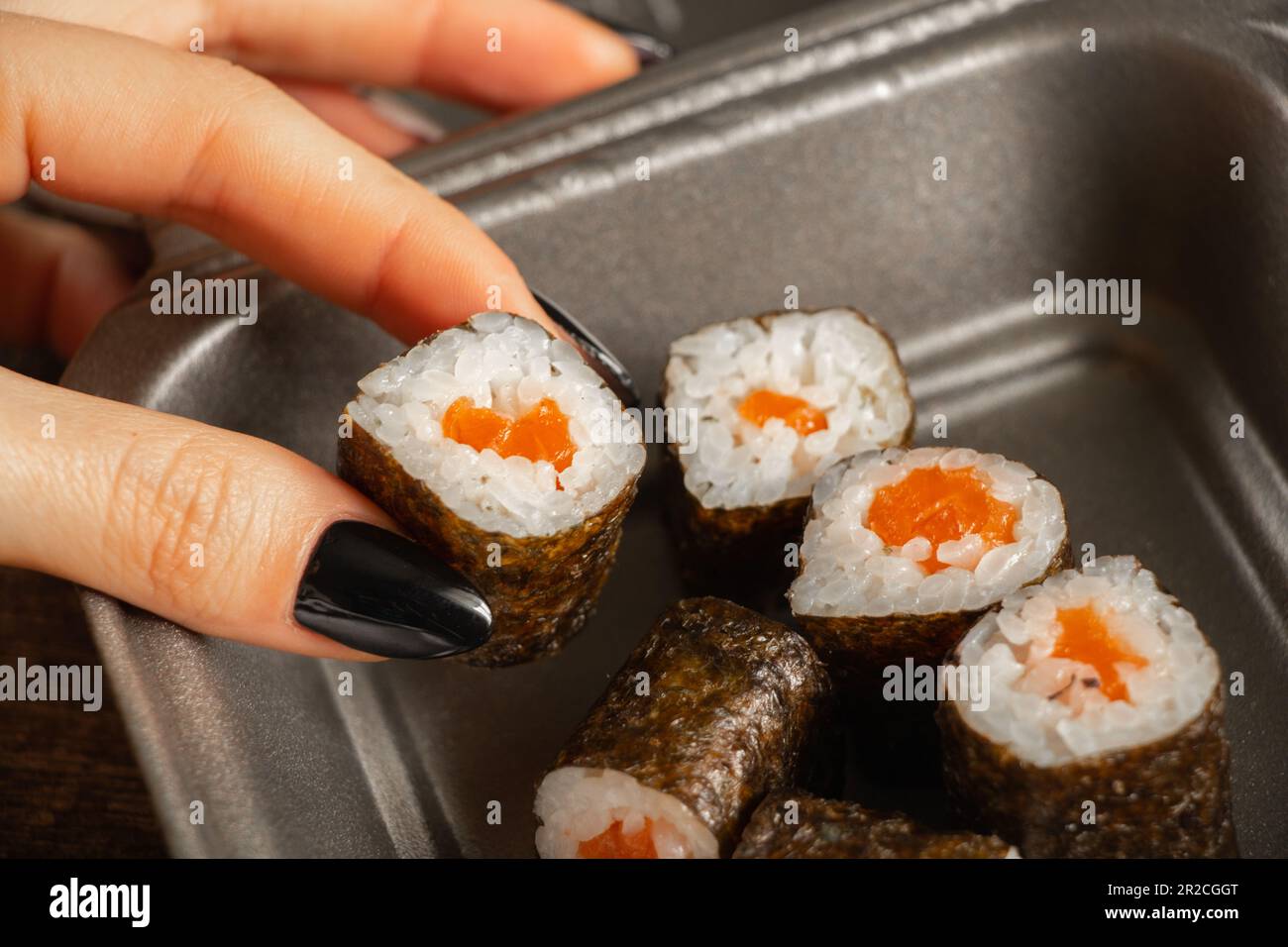 Weibliche Finger kommen aus der Essensbox Sushi mit Lachs auf Holzhintergrund, Nahaufnahme, Restaurant-Essen Stockfoto