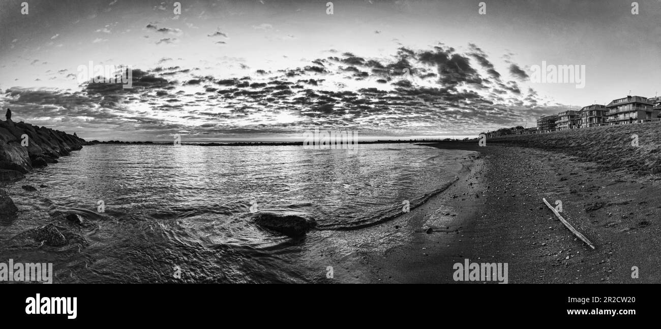 Die Sonne geht langsam zum Horizont hinab und wirft ein warmes Licht über das ruhige Wasser Roms und die Skyline der Promenade mit dem mit kleinen Wolken bemalten Himmel Stockfoto