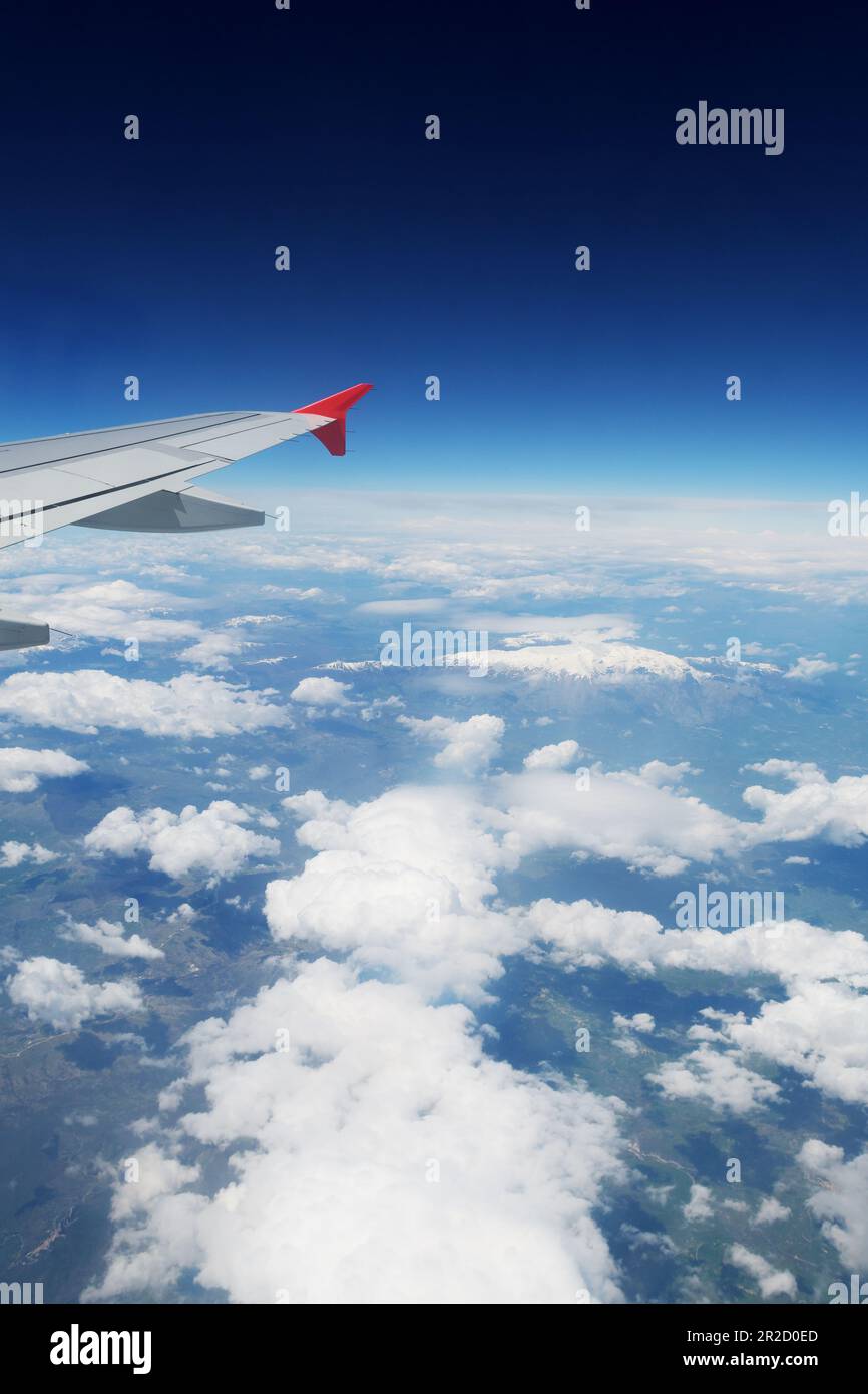 Ein Blick durch ein Flugzeugfenster während des Fluges. Sichtbarer Flügel, Wolken über Land und Raum. Flugreisen-, Transport- und Tourismuskonzepte. Stockfoto