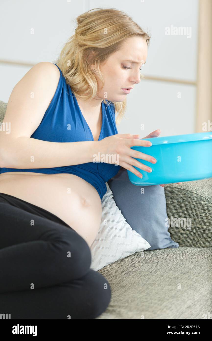 Schwangere Frau auf dem Sofa, die eine Plastikschüssel in der Hand hält Stockfoto