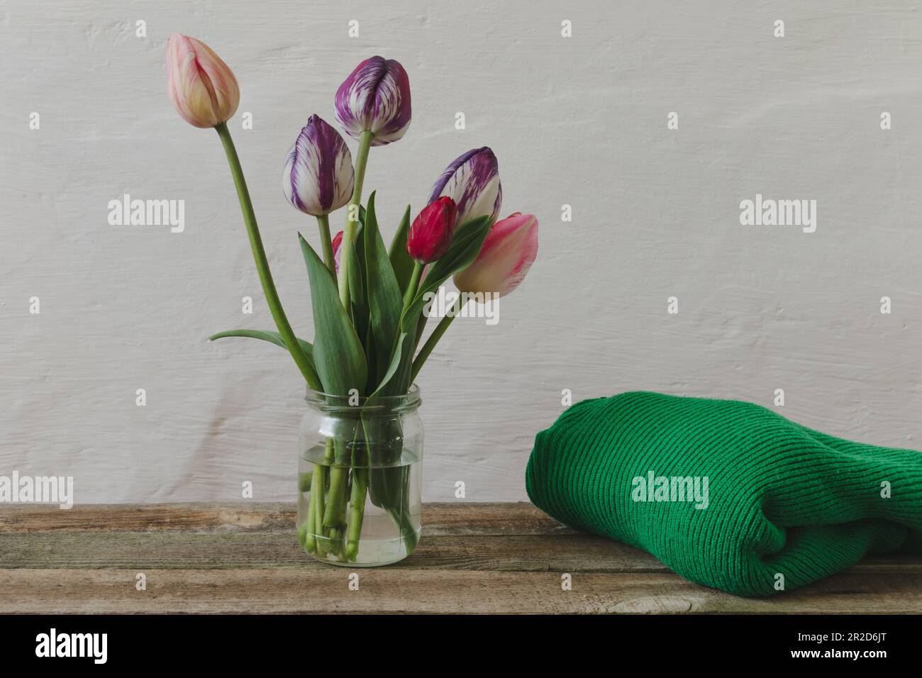 Ein Strauß Tulpen und ein Pullover auf einem Holztisch. Stockfoto