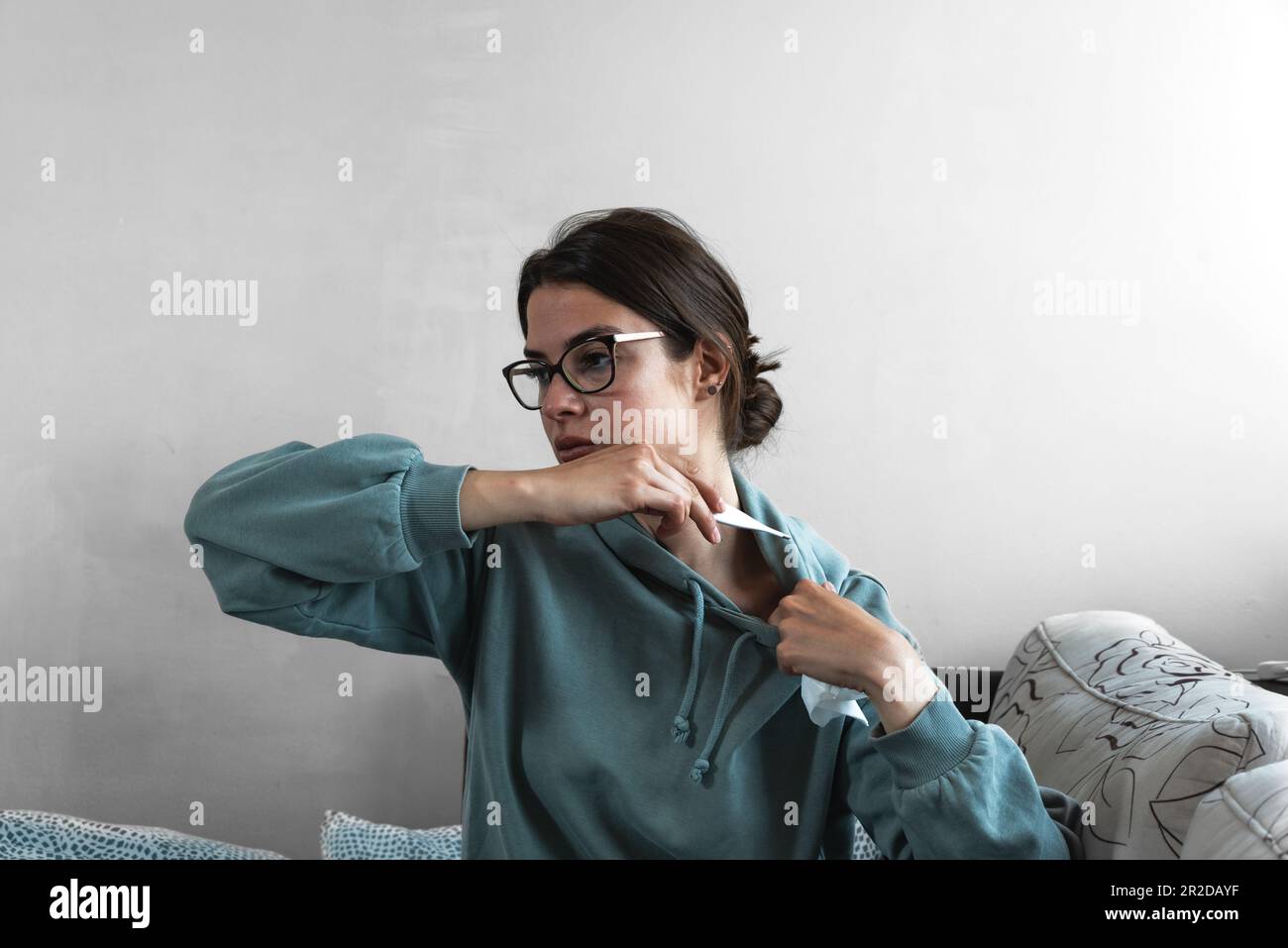 Eine kranke junge Frau, die auf dem Sofa saß und mit einer Decke übersät war, die eiskalt die Nase blaste, bekam Fieber, Schnupfen, Niesen im Gewebe, krankes Mädchen, das reinkam Stockfoto