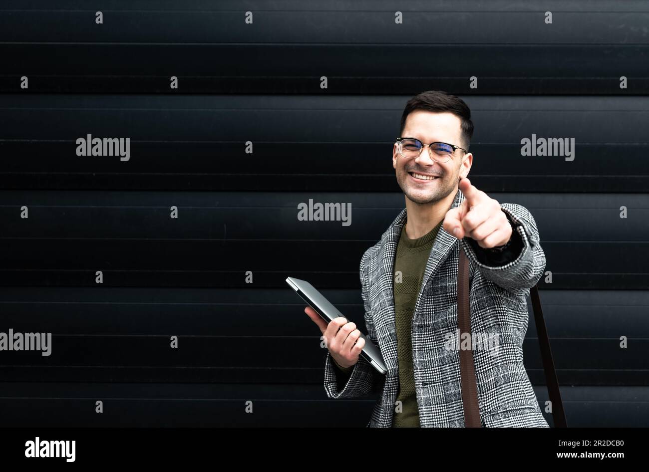 Junger, glücklicher, erfolgreicher Geschäftsmann, der nach einem großartigen Arbeitstag und Erfolg der Mitarbeiter vor dem Bürogebäude lächelt und mit dem Finger auf die Kamera zeigt Stockfoto