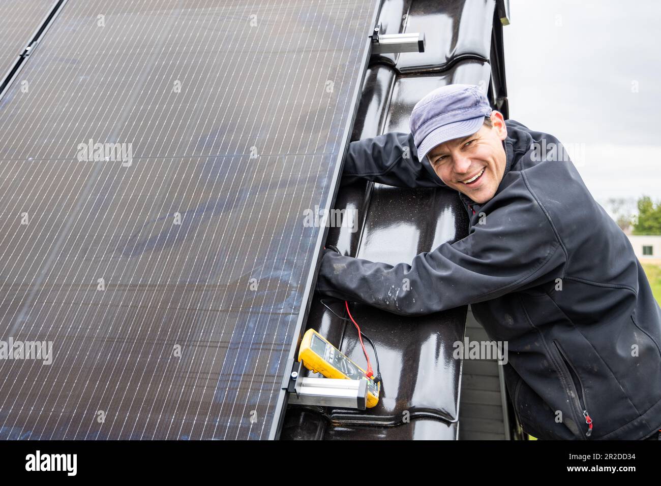 Lächelnder Techniker, der an der Installation eines Solarmoduls auf einem Dach arbeitet Stockfoto