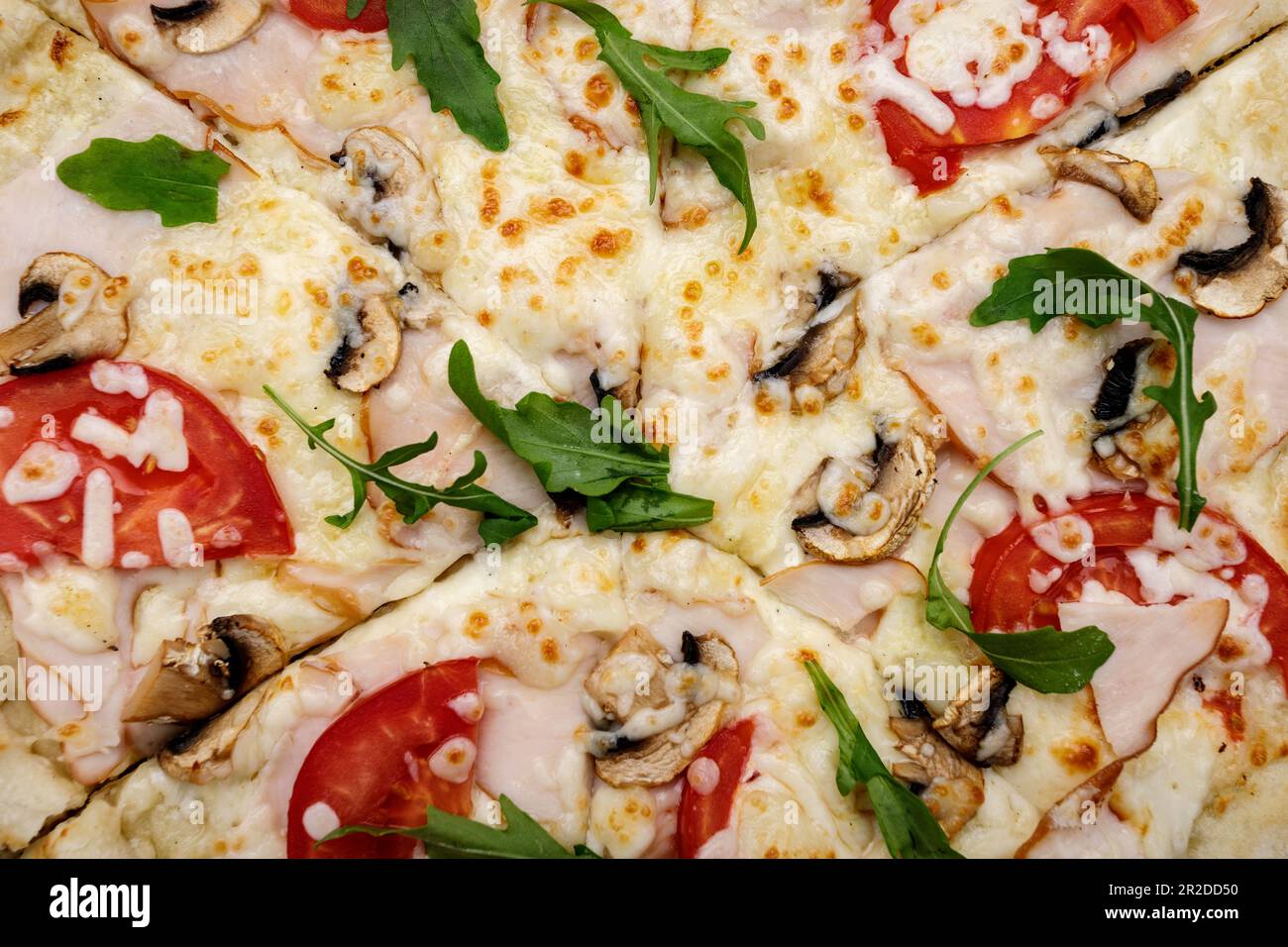 Geräucherte Fleisch- und Käsepizza, garniert mit Tomaten, Rucola und Pilzen, Nahaufnahme Stockfoto