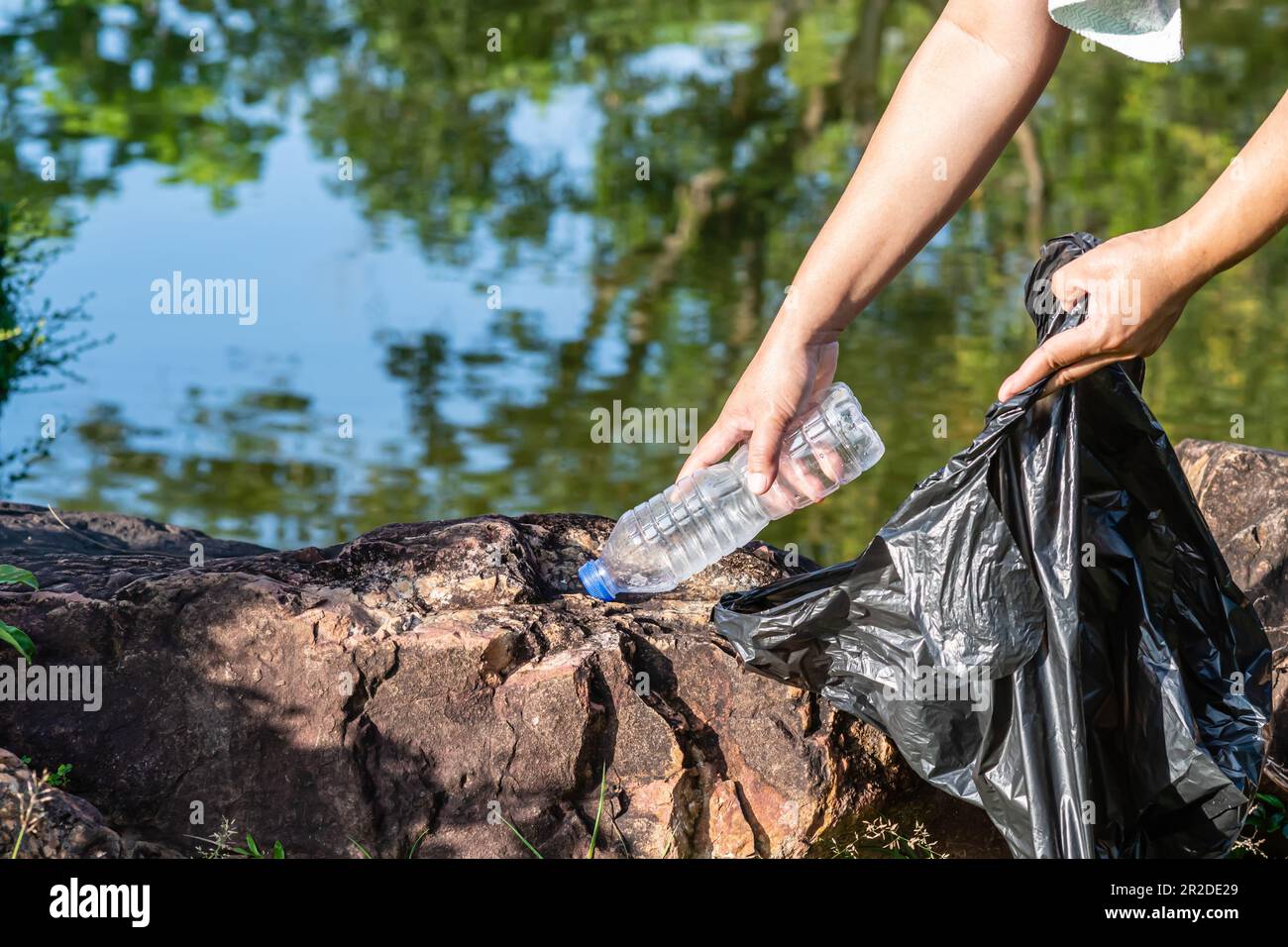 Eine Frau putzt, indem sie Plastikflaschen an einem natürlichen Wasserreservoir aufnimmt. Konzept des Umweltschutzes, der Rettung der Welt, des Recyclings, des redu Stockfoto